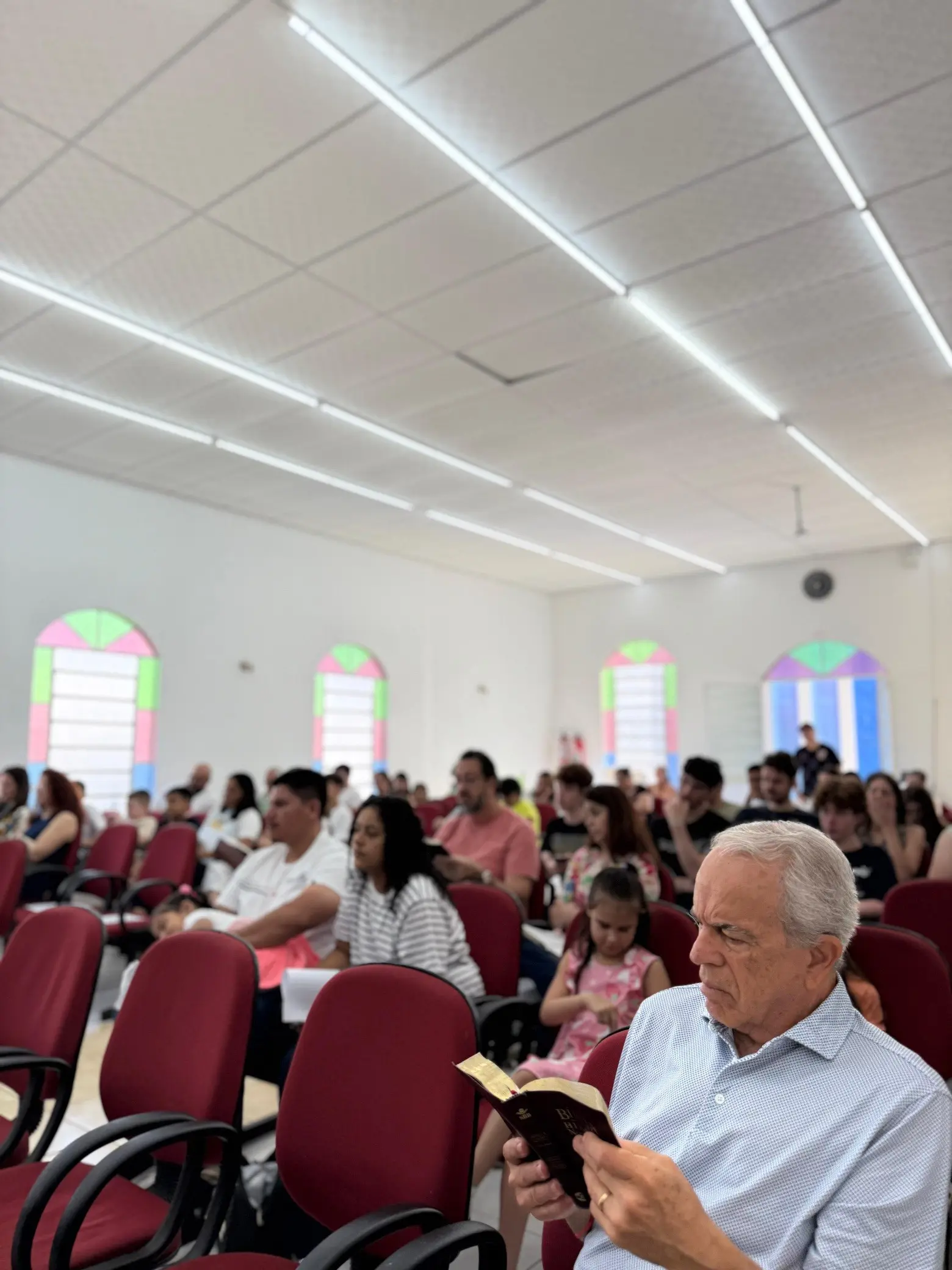 Senhor lendo a Bíblia durante a Escola Dominical, com a classe ao fundo
