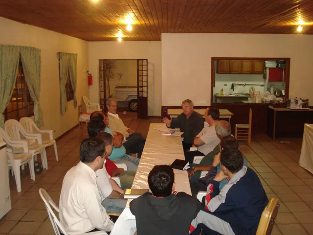 Homens reunidos ao redor de uma mesa comprida no salão social