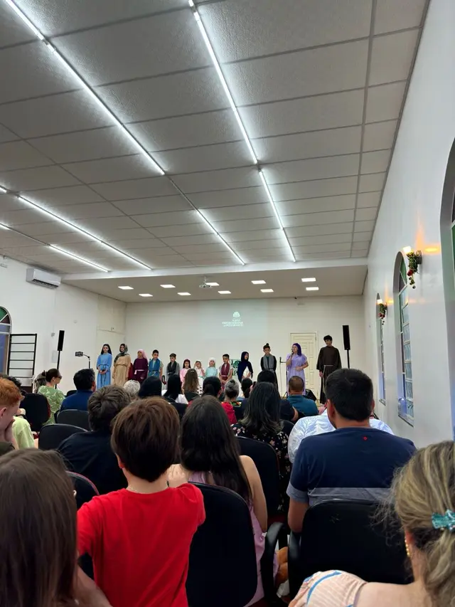 Crianças e adolescentes com roupas de personagens bíblicos no palco, diante do templo cheio