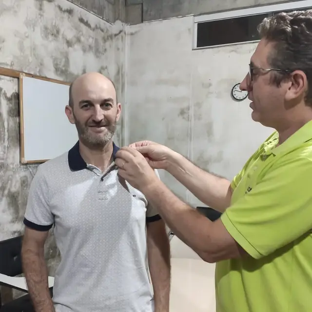 Um homem de camisa verde coloca o broche da UPH na gola de outro, que sorri