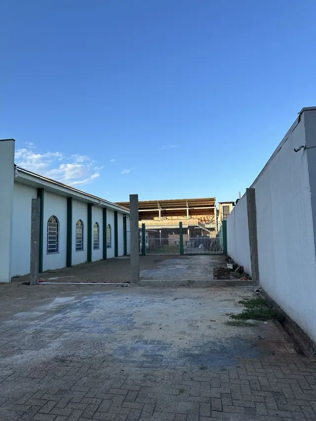 Pátio da igreja com os pilares de concreto do novo portão e o templo de janelas em arco ao lado