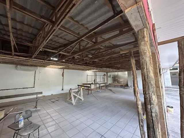 Salão social em obra, sem o forro, com o madeiramento do telhado à mostra e cavaletes sobre o piso