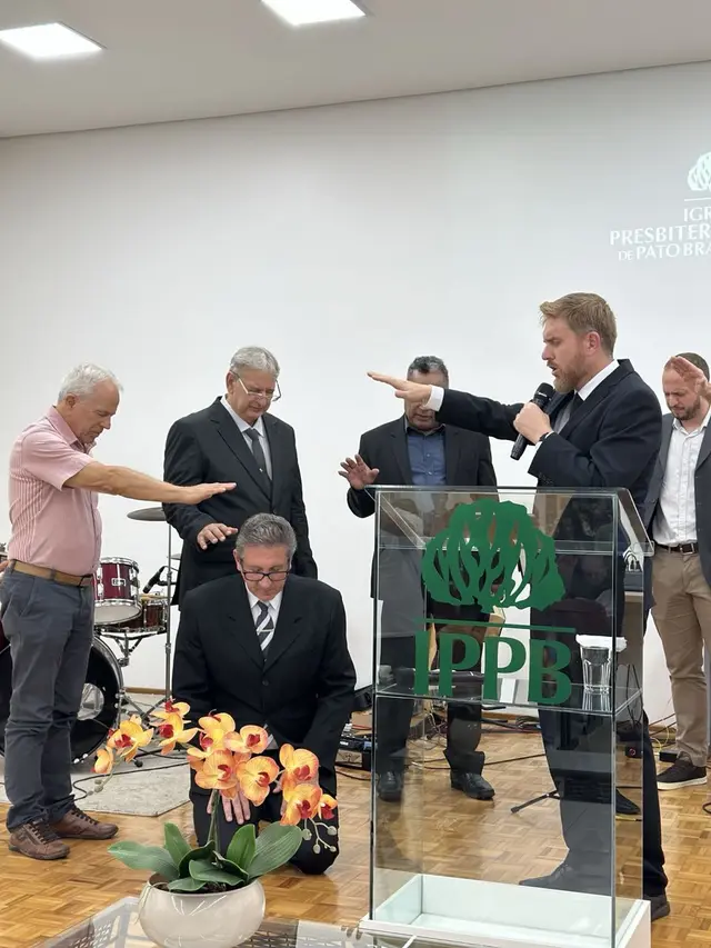 Rev. Maurício ajoelhado diante do púlpito enquanto pastores estendem as mãos sobre ele em oração