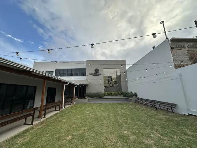 Prédio novo pronto, com o letreiro da igreja, e o pátio gramado com bancos e varal de luzes