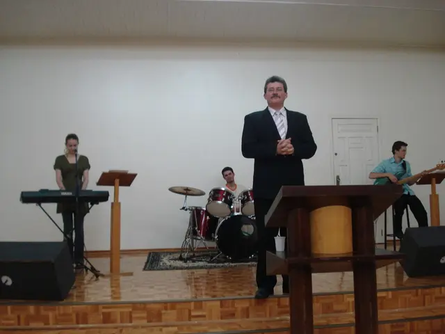 Pastor Ademir Colpani de pé no púlpito do templo, com o grupo de louvor atrás: teclado, bateria e baixo