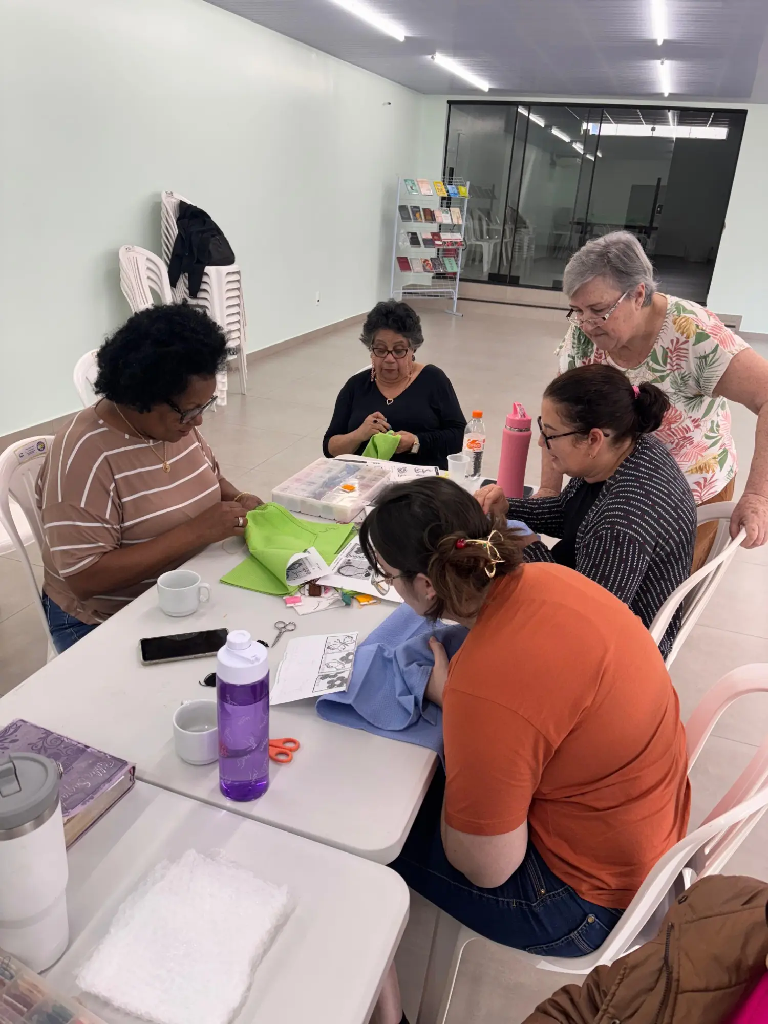 Mulheres da igreja reunidas em volta da mesa bordando panos de prato, com linhas e moldes de desenho