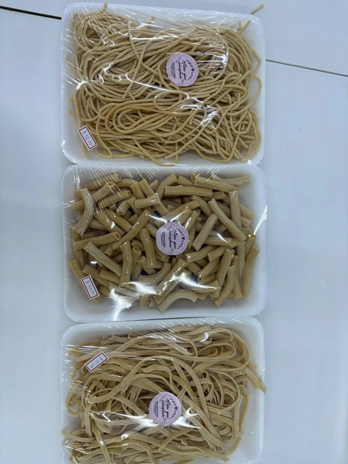 Três bandejas de macarrão caseiro embaladas com o selo do Mãos que Abençoam: espaguete, macarrão curto e talharim