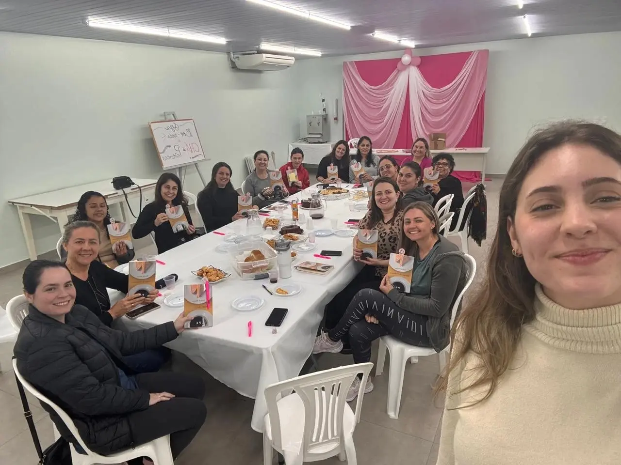 Mulheres do Café Literário à mesa com lanche, segurando o livro que estão lendo, no salão social da IPPB