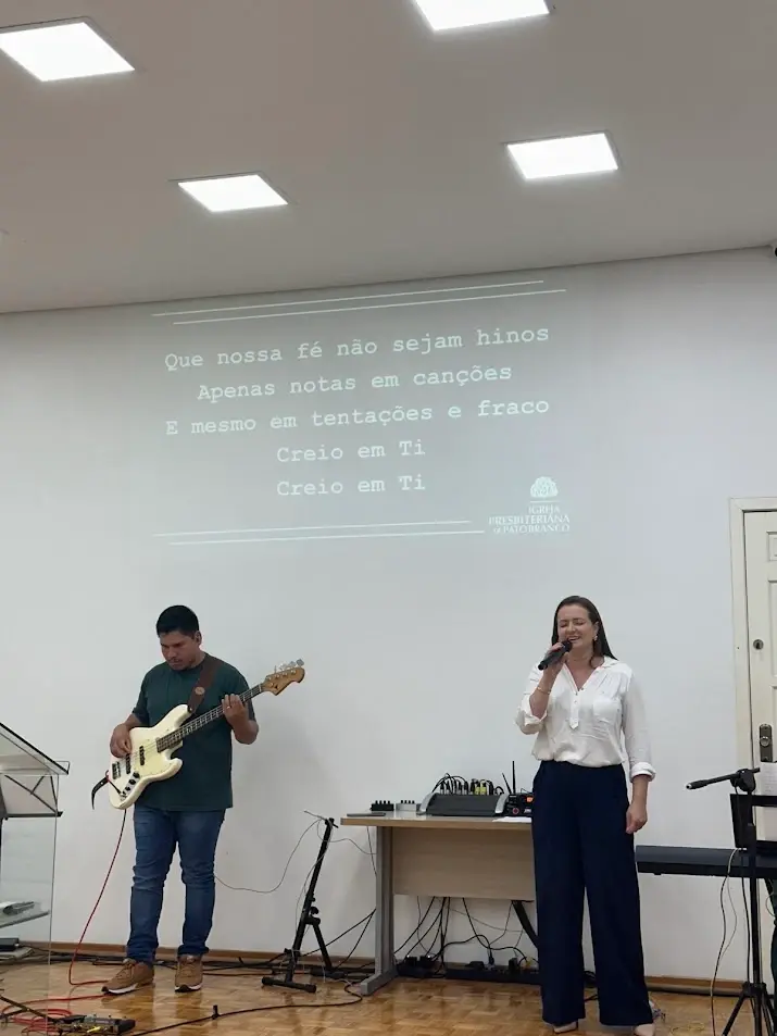 Baixista e cantora do Ministério de Louvor conduzindo o canto, com a letra projetada no telão
