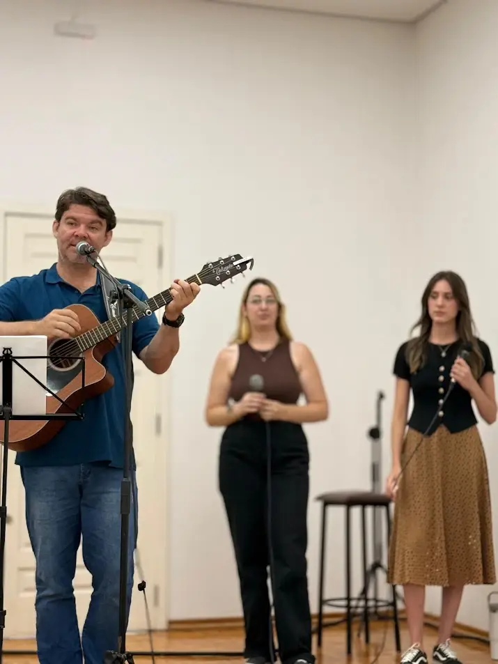 Músico tocando violão acompanhado por duas cantoras do Ministério de Louvor