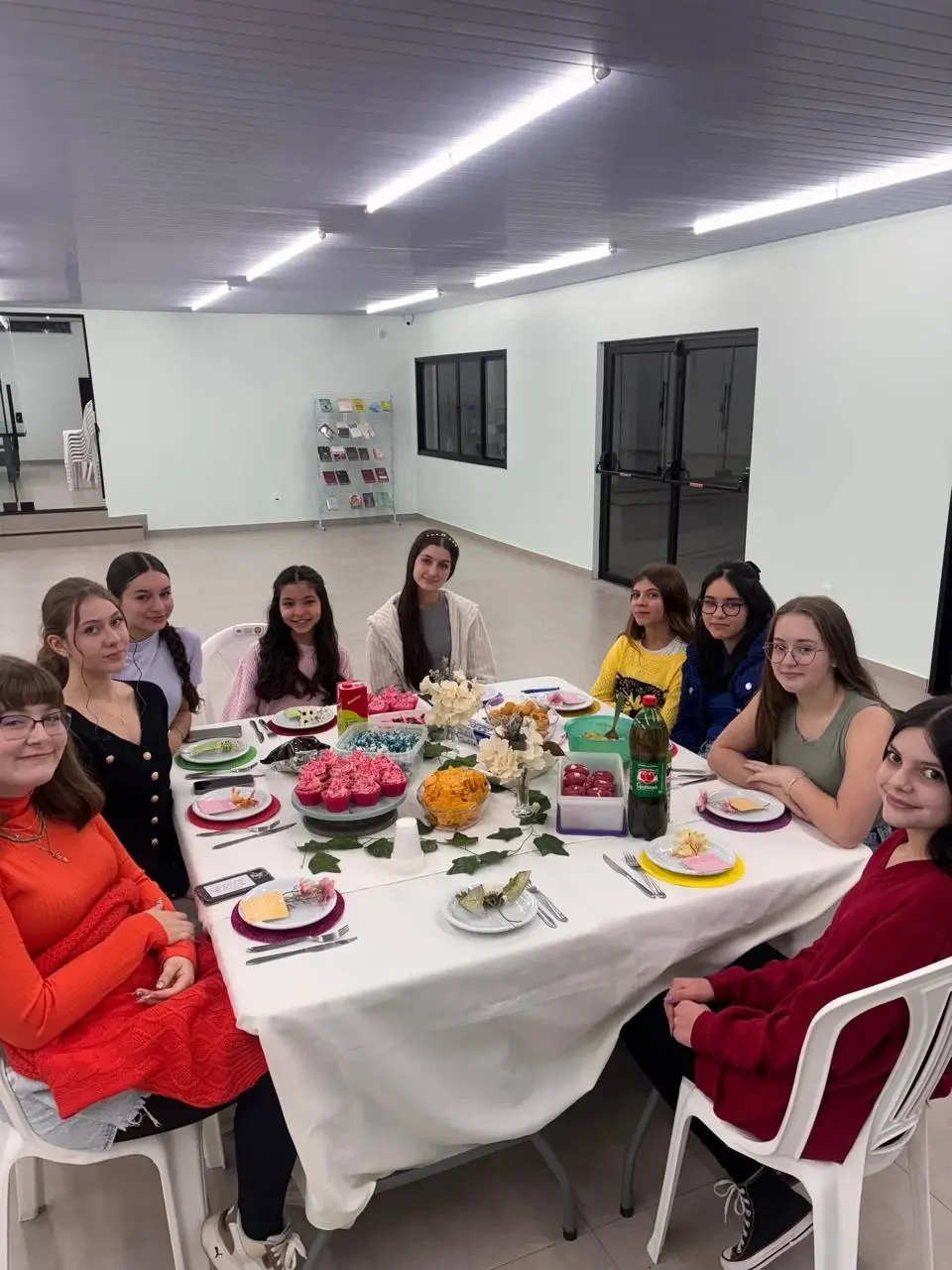 Meninas à mesa decorada com flores, cupcakes e lanche em um encontro especial do Só Meninas
