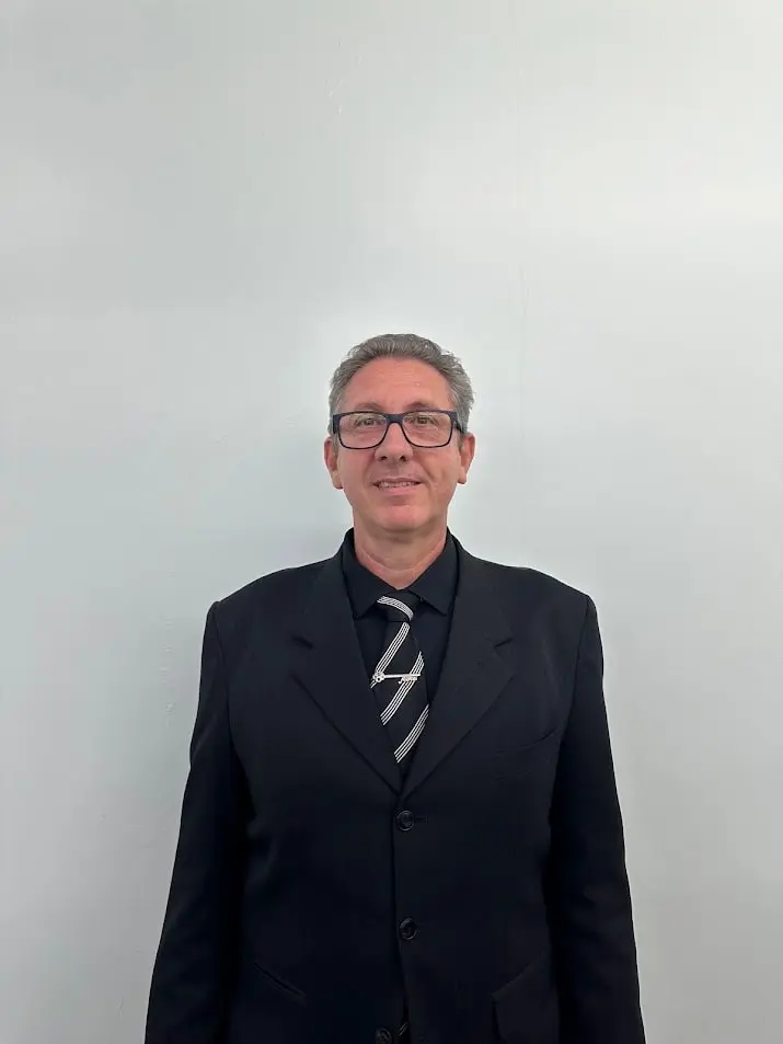Rev. Maurício Alfredo Vicari, pastor titular da IPPB, de terno preto, gravata listrada e óculos, sorrindo diante de uma parede clara