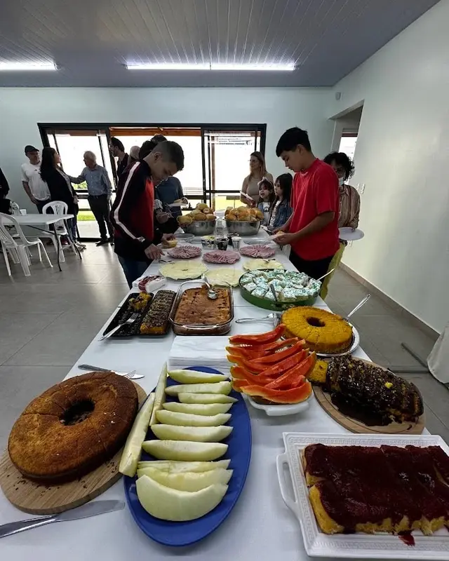 Mesa de café da comunhão, com bolos e frutas, e irmãos se servindo