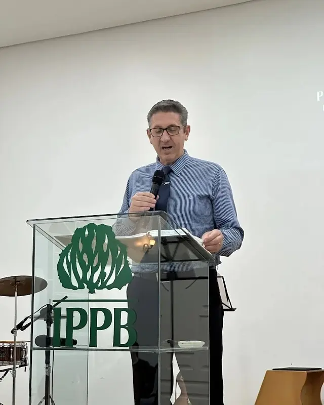 Pregador lendo a Bíblia no púlpito de acrílico com a marca da IPPB