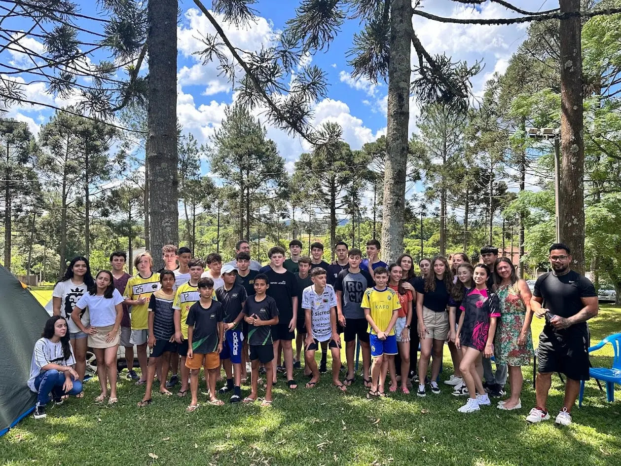Adolescentes da UPA em um acampamento, reunidos num gramado entre araucárias, ao lado de uma barraca